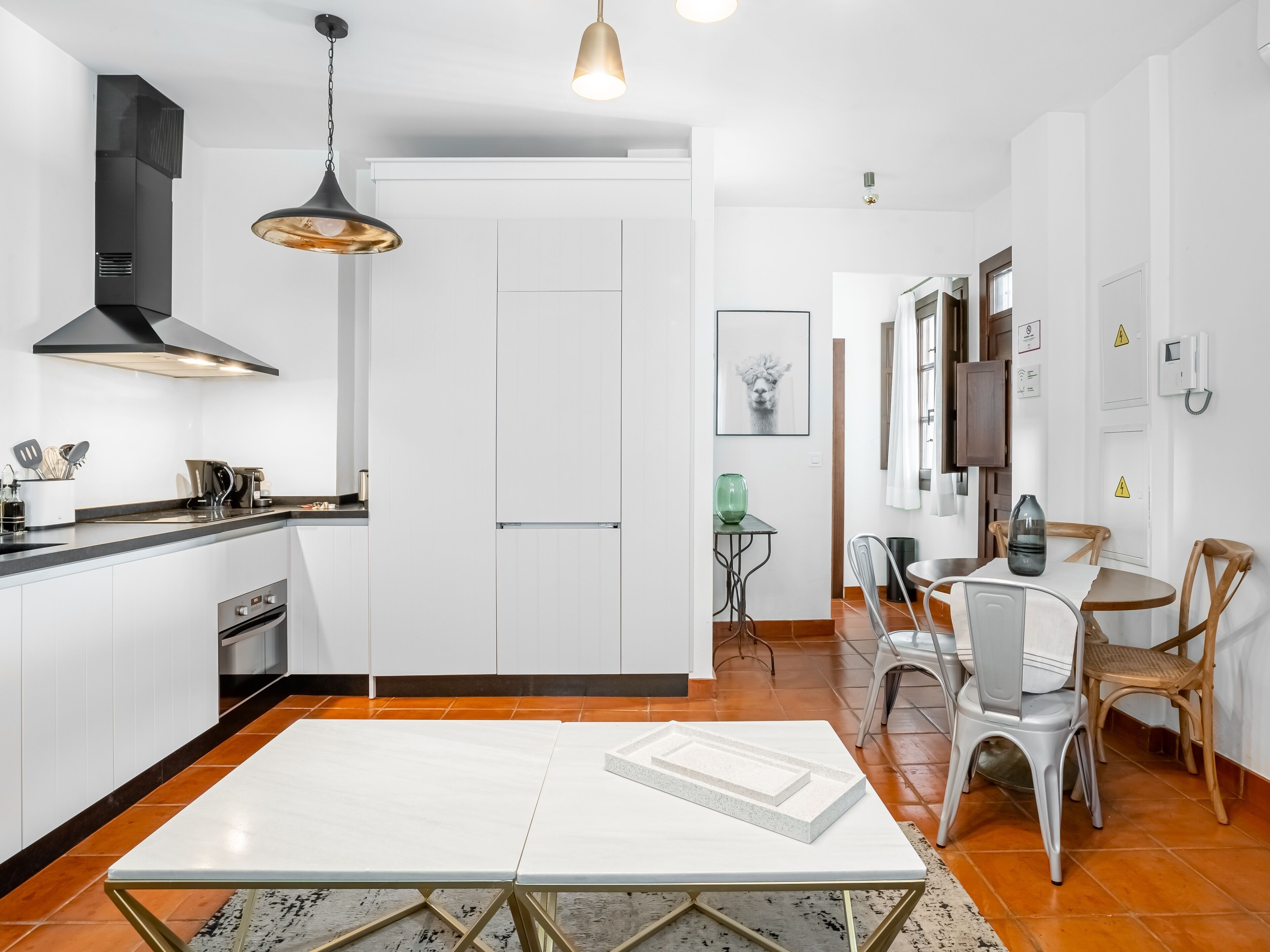 Una cocina moderna con armarios blancos, una campana extractora negra y una lámpara colgante.