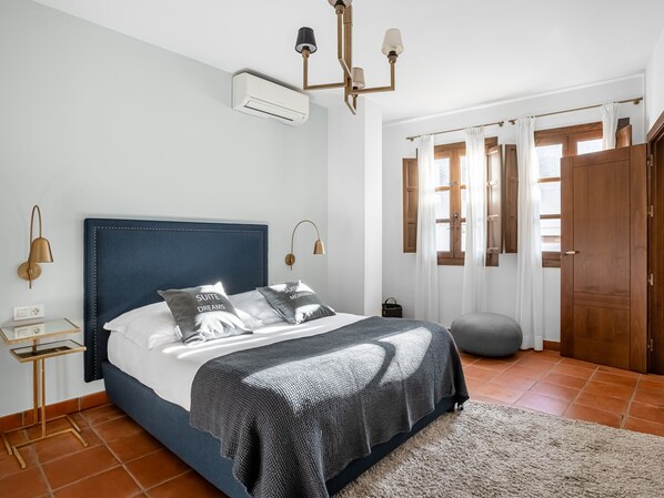 Ein Schlafzimmer mit einem Bett, Nachttischlampen, einem Nachttisch, einem Fenster mit Vorhängen und einer Tür.