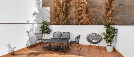 Un patio con suelo de baldosas, una mesa con sillas y dos macetas.