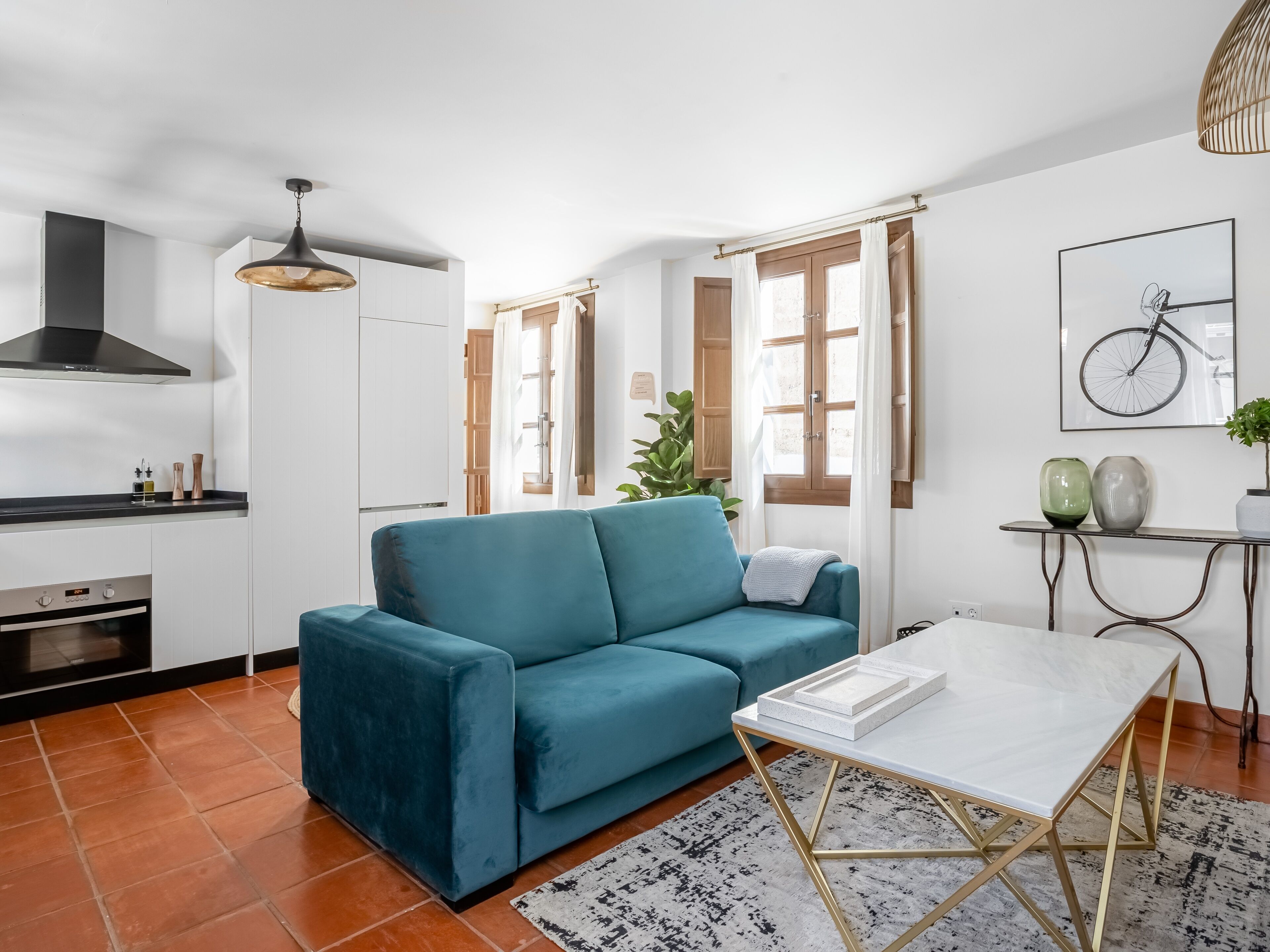 Una sala de estar moderna con un sofá azul verdoso, una mesa de centro blanca y una cocina con armarios blancos y una estufa negra.