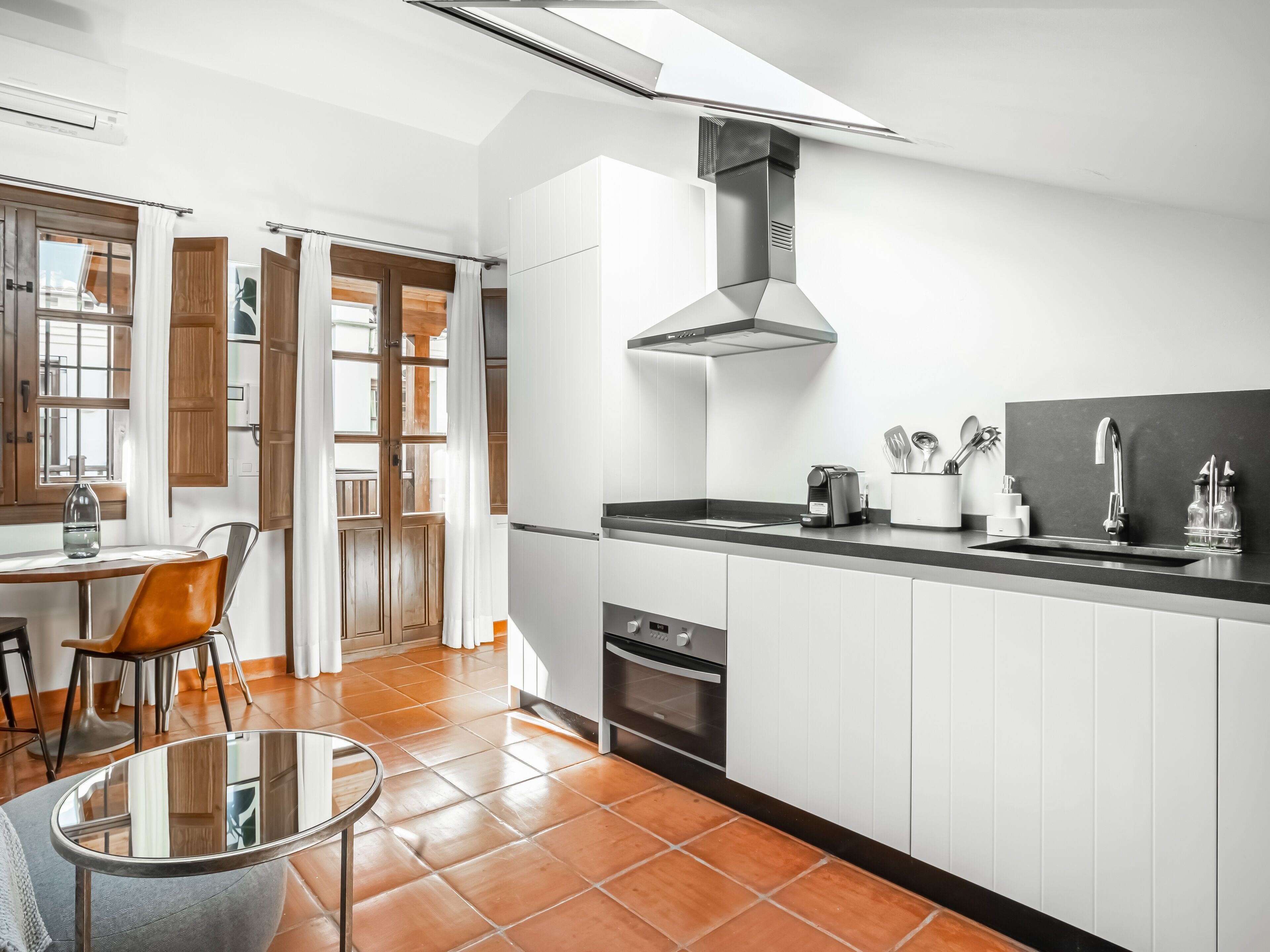 Een moderne keuken met witte kasten, een zwart aanrecht en een rvs afzuigkap.