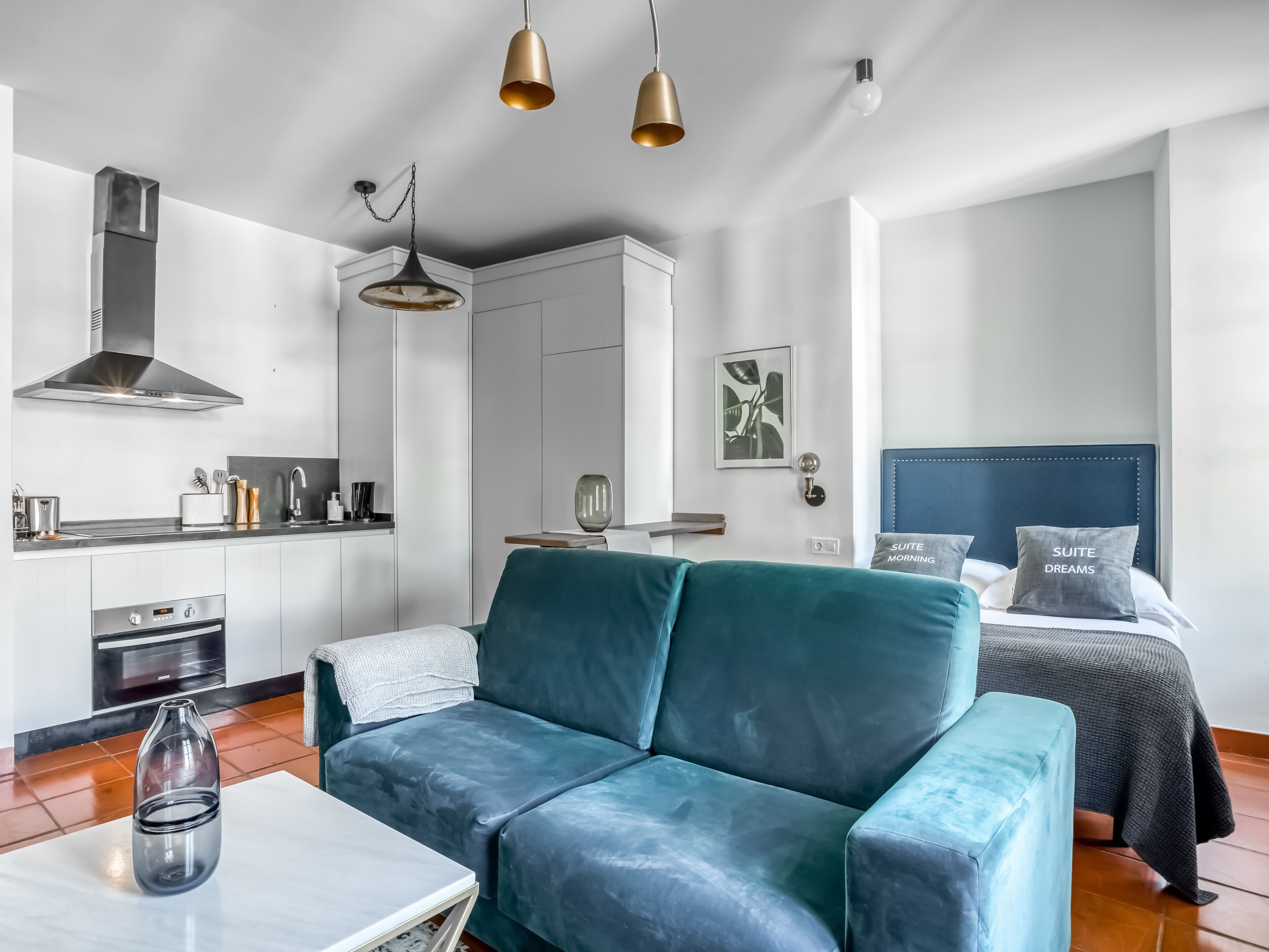 Une pièce moderne et bien éclairée, comprenant un canapé, un lit avec des oreillers, un coin cuisine et une table à manger.