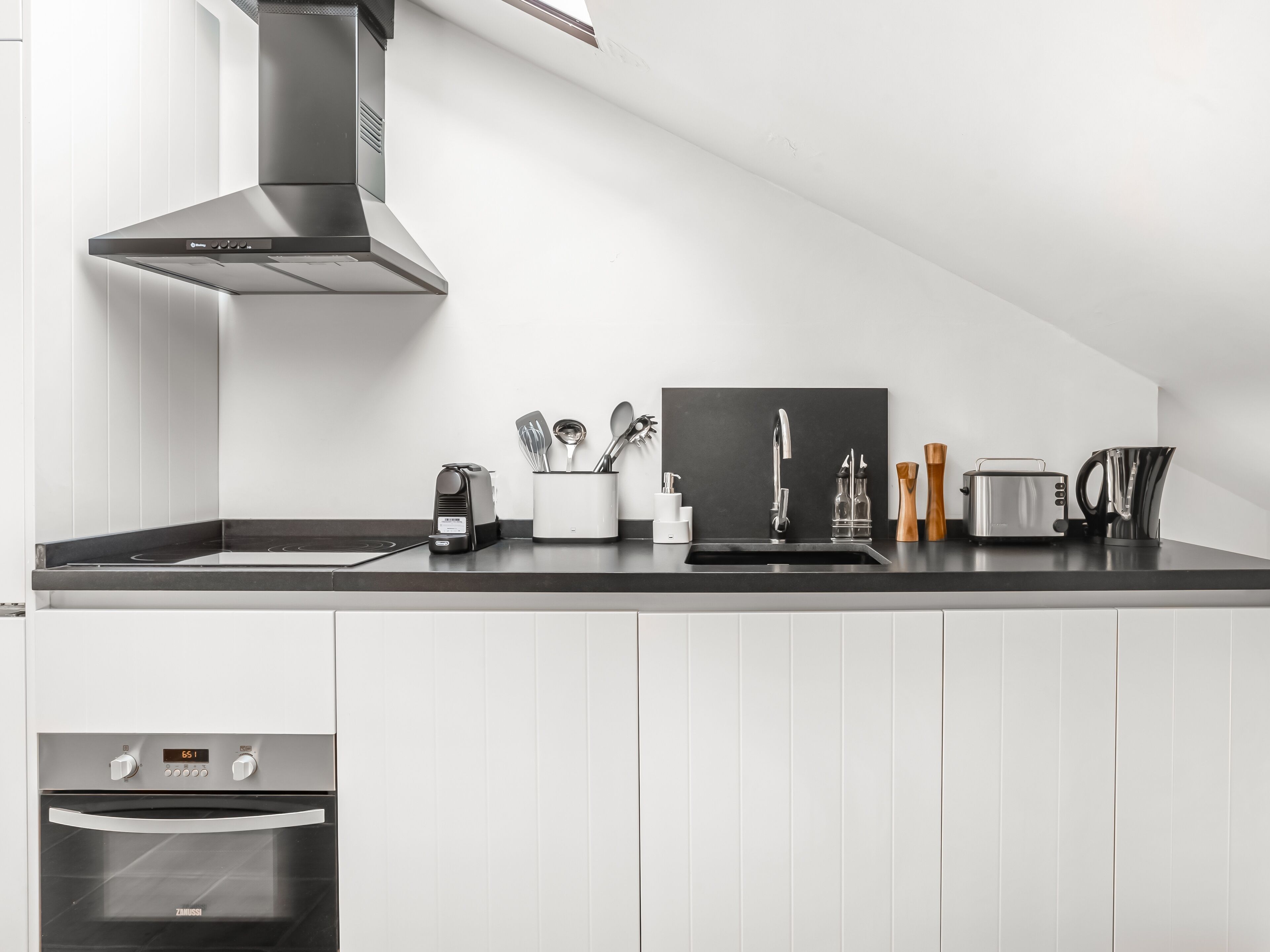 Een moderne keuken met een ingebouwde oven, een roestvrijstalen afzuigkap, een zwart aanrecht en een zwarte spoelbak.