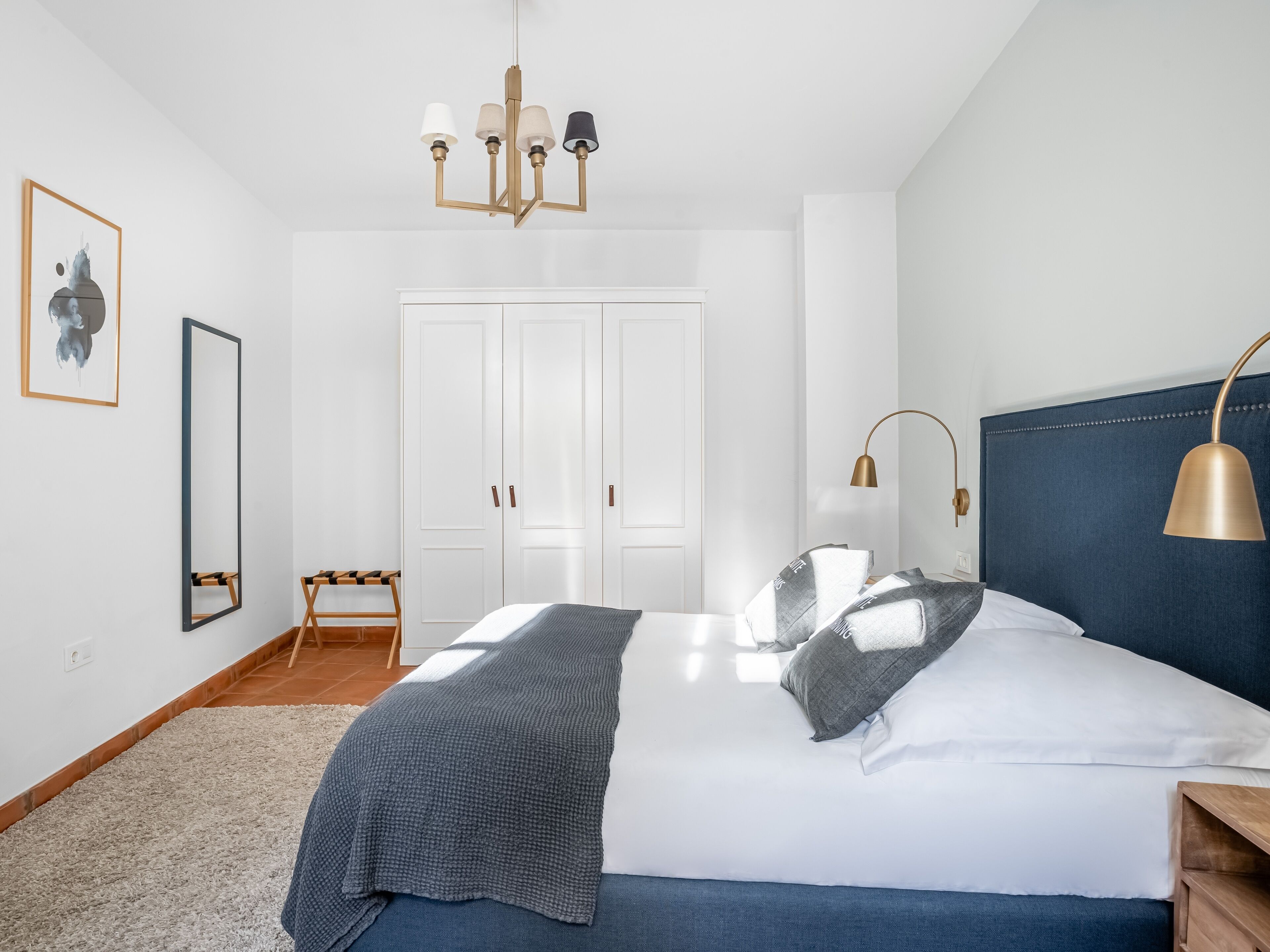 Une chambre à coucher avec un lit, des tables de chevet, une armoire, un miroir et un lustre.