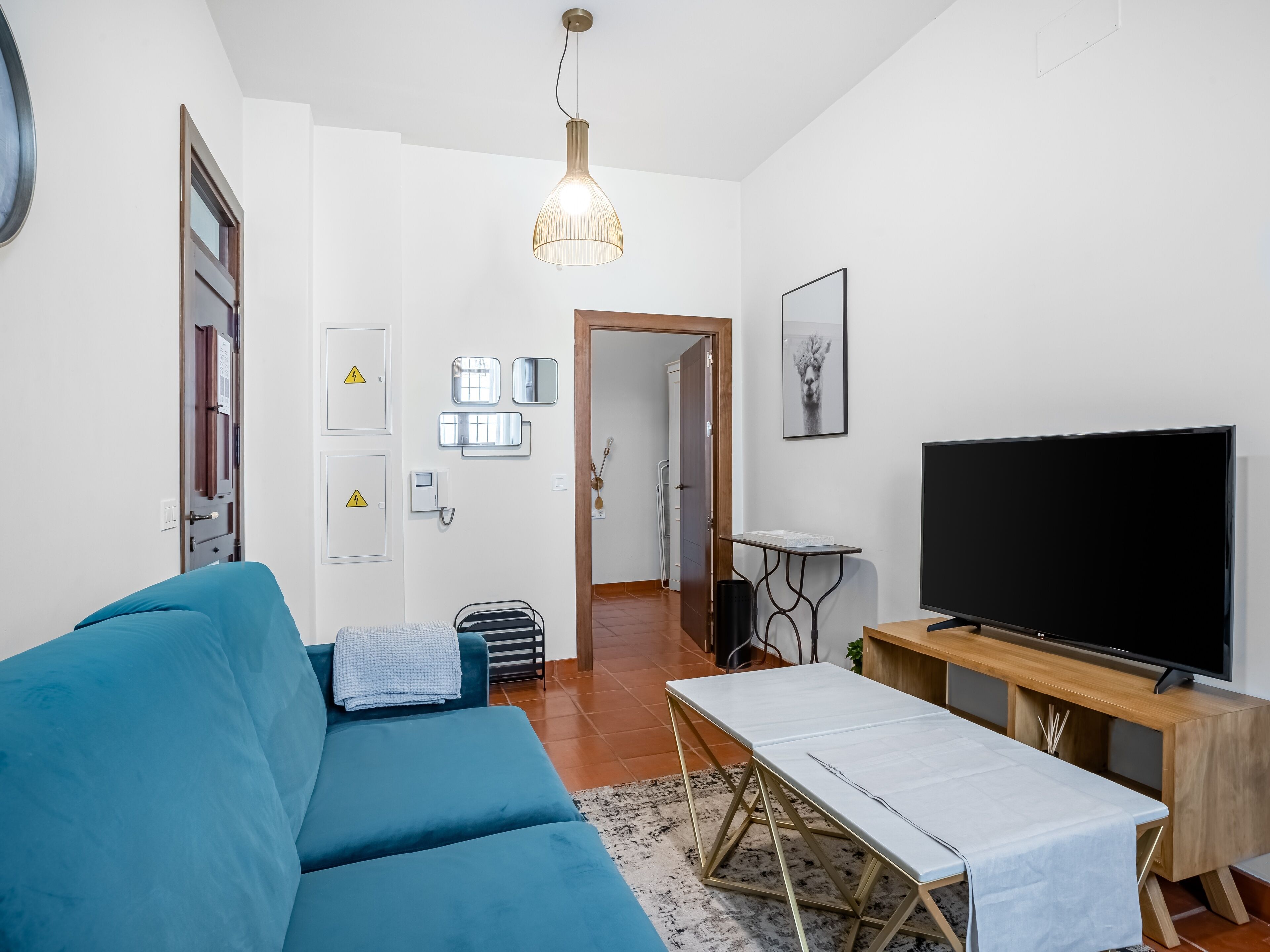 Una sala de estar moderna con un sofá azul, un televisor sobre un mueble de madera y una mesa de comedor con mantel blanco.