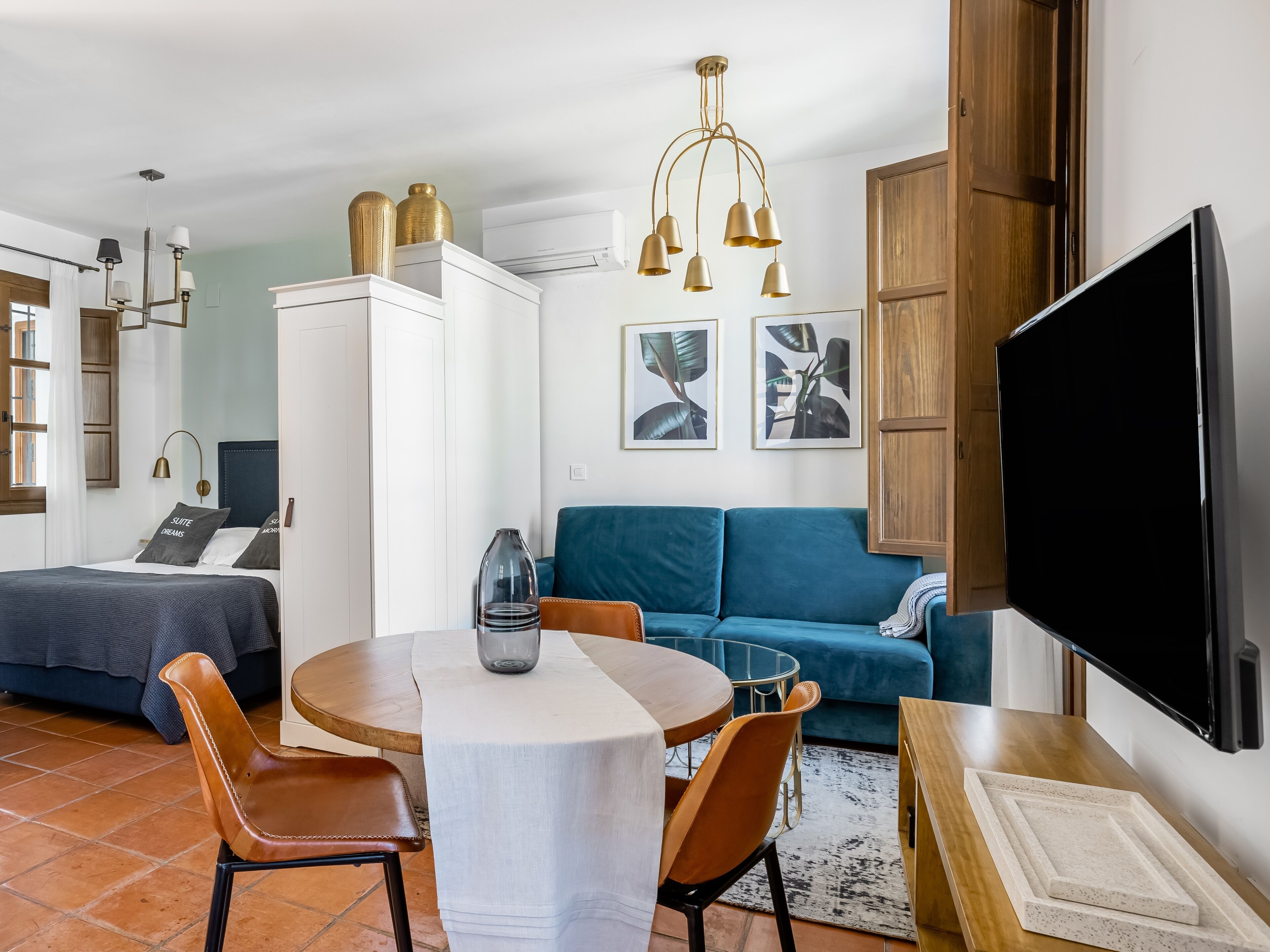 Ein modernes Wohnzimmer mit einer Couch, einem Esstisch mit Stühlen, einem Fernseher und einem großen Fenster.