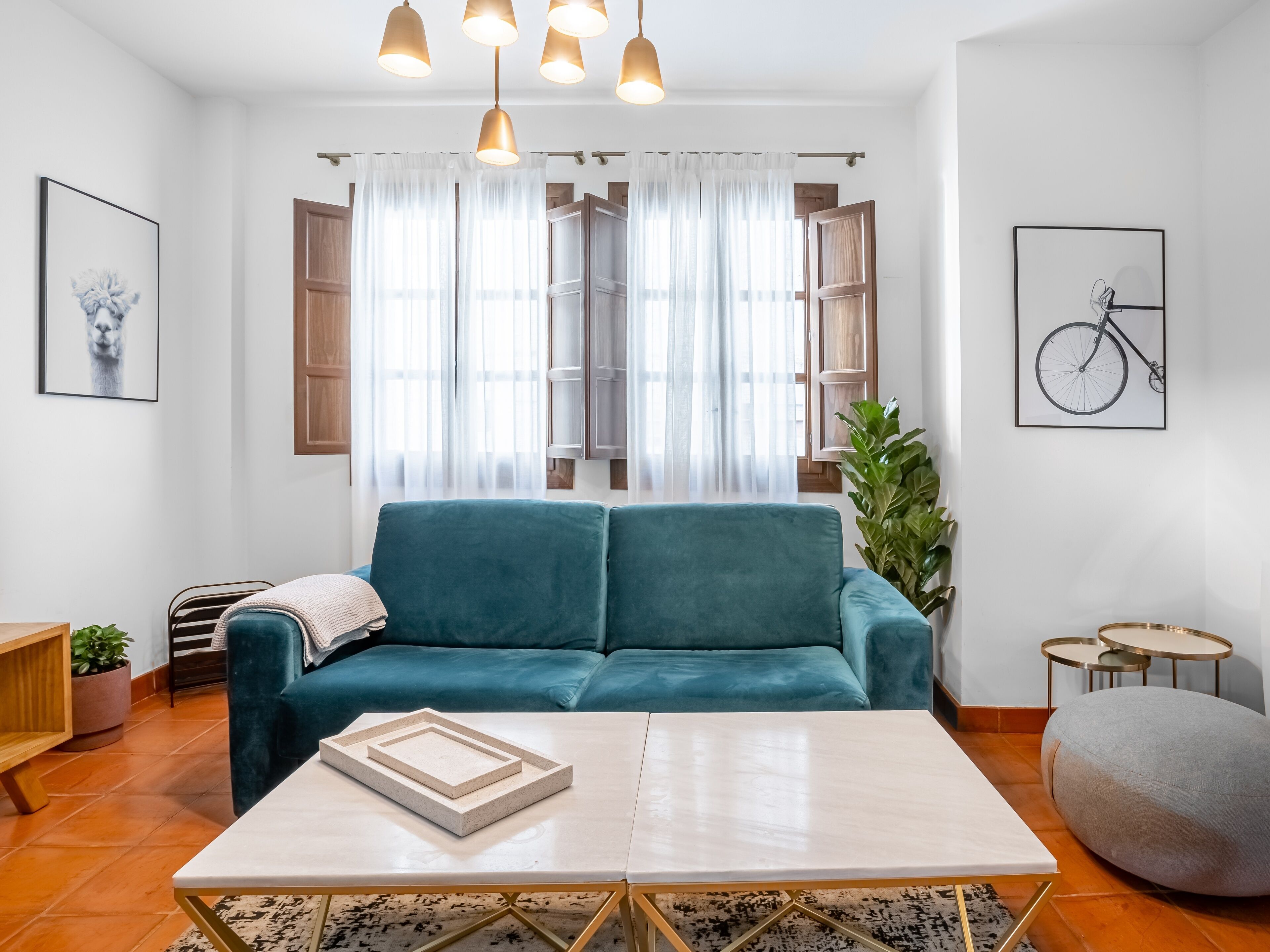 A modern living room with a teal sofa, a white coffee table, and a large window with sheer curtains.