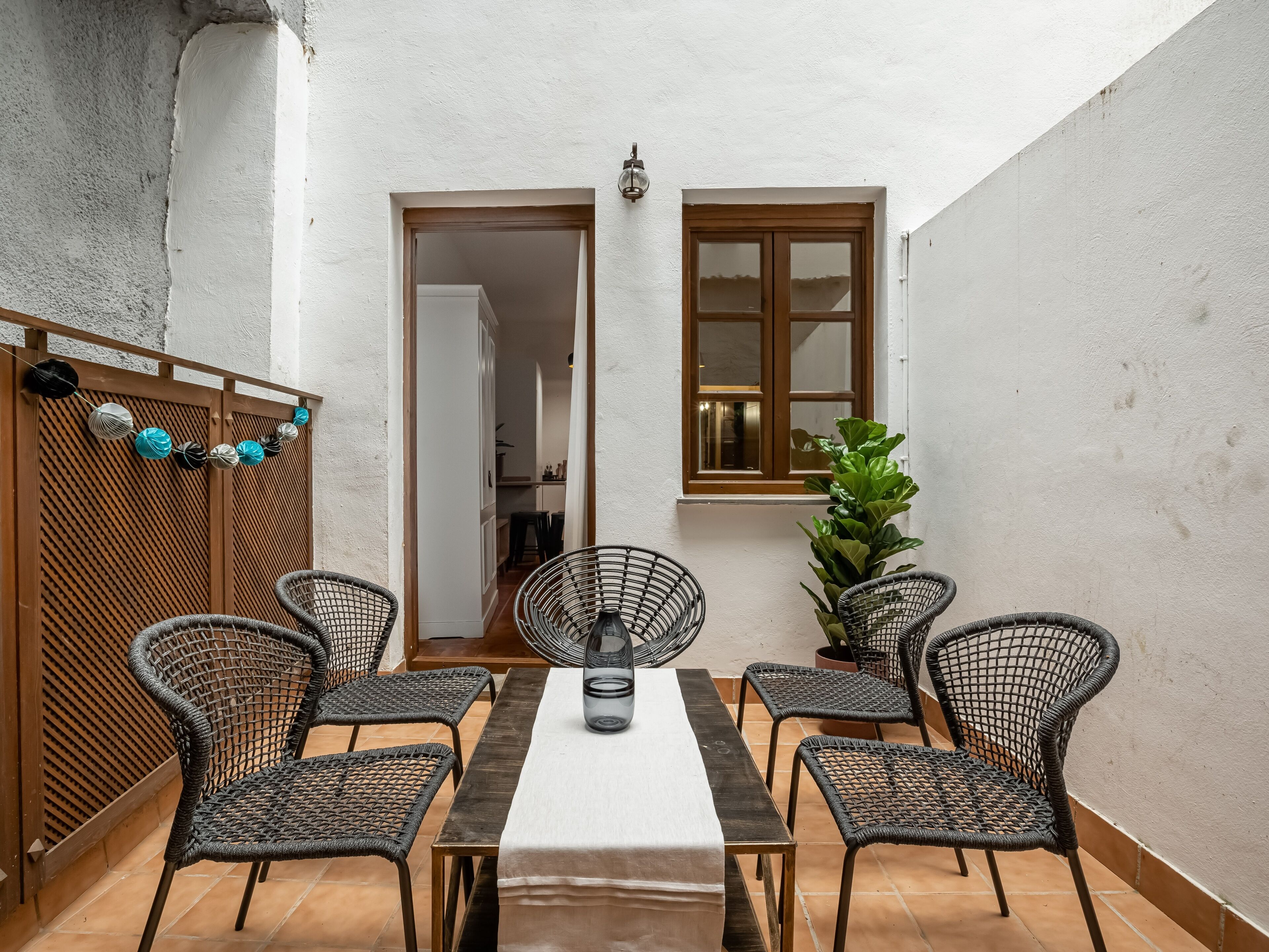 Un patio con una mesa y cuatro sillas de mimbre, una valla de madera y una planta en maceta.