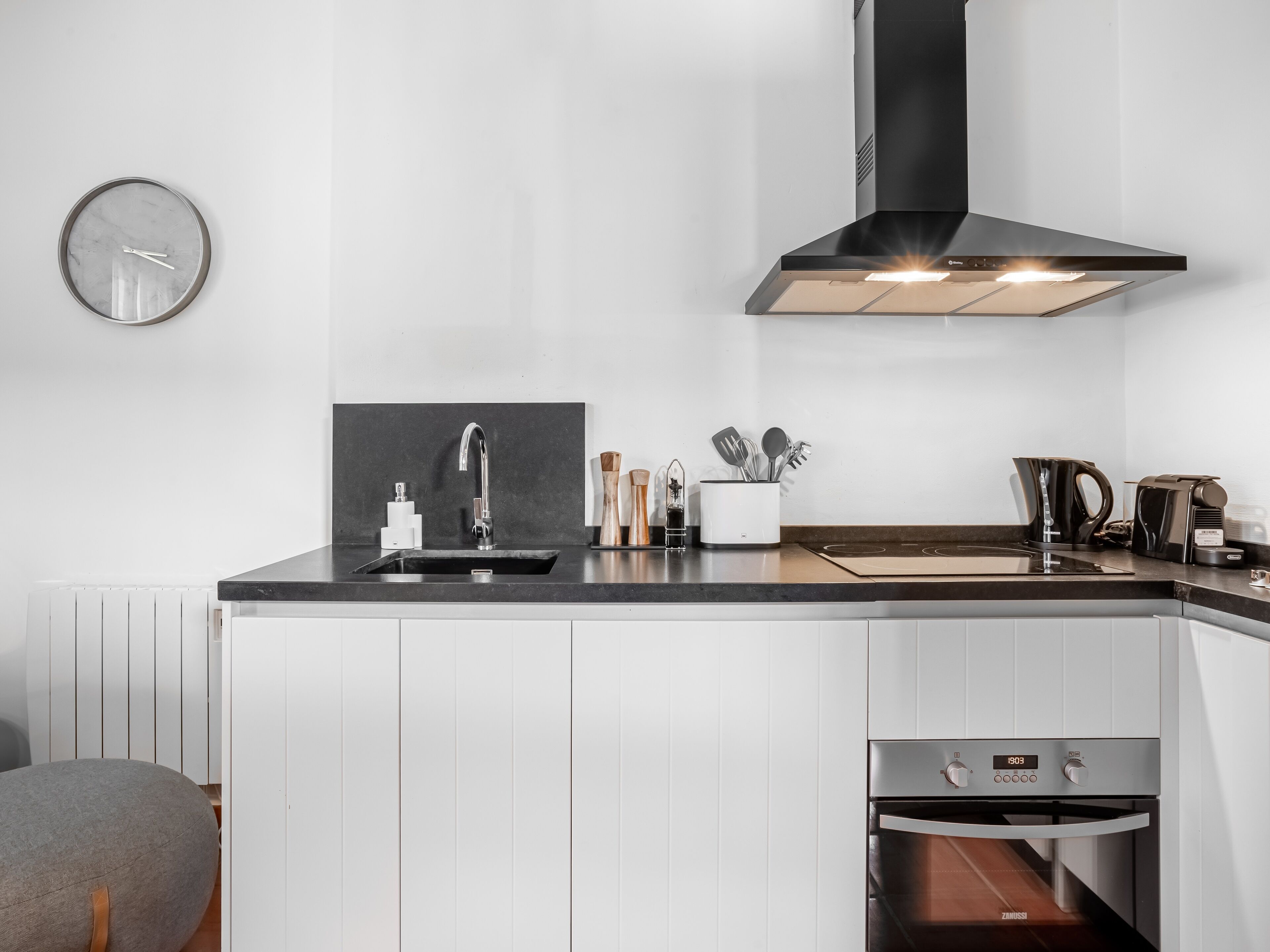 Eine moderne Küche mit schwarzem Arbeitsplatz, weißen Schränken, einer Edelstahl-Spüle, einem eingebauten Backofen und einer schwarzen Dunstabzugshaube.