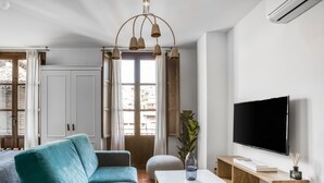 Ein modernes Wohnzimmer mit einem türkisfarbenen Sofa, einem Couchtisch, einem Fernseher und einem großen Fenster mit Vorhängen.