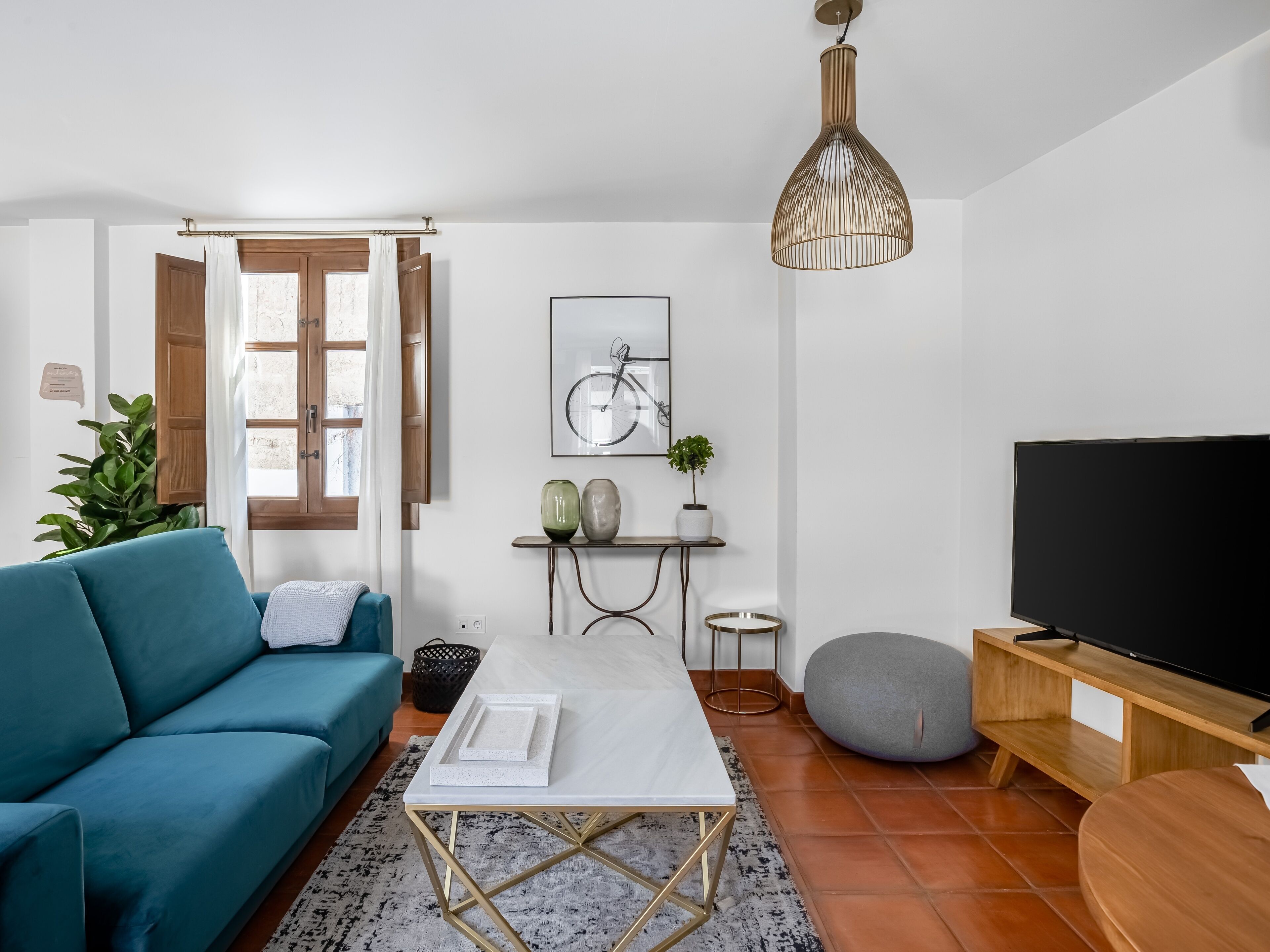 Ein modernes Wohnzimmer mit einem türkisfarbenen Sofa, einem weißen Couchtisch, einem Fernseher und einem großen Fenster mit Vorhängen.