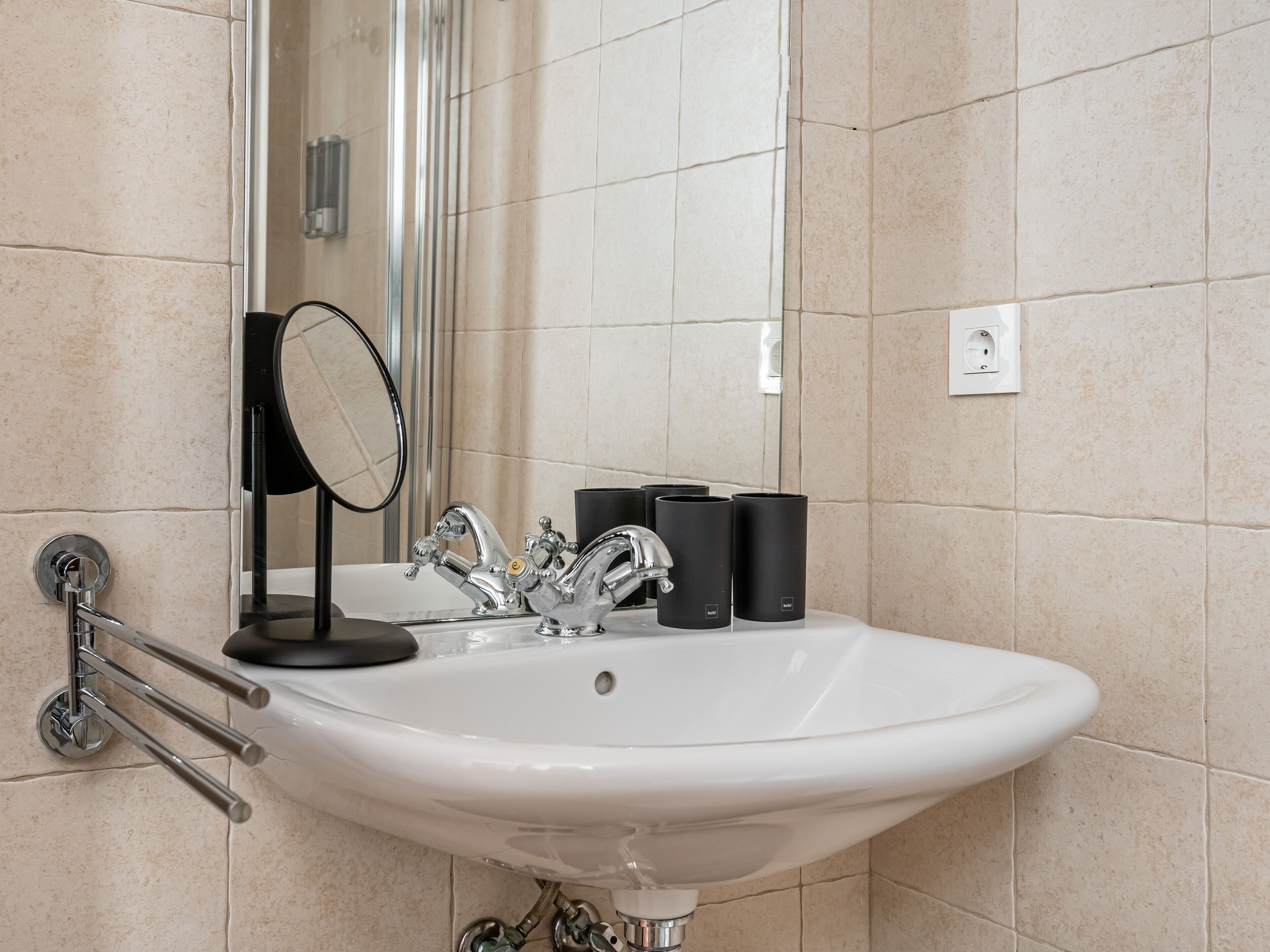 Un baño con un lavamanos blanco, un espejo y un perchero para toallas.