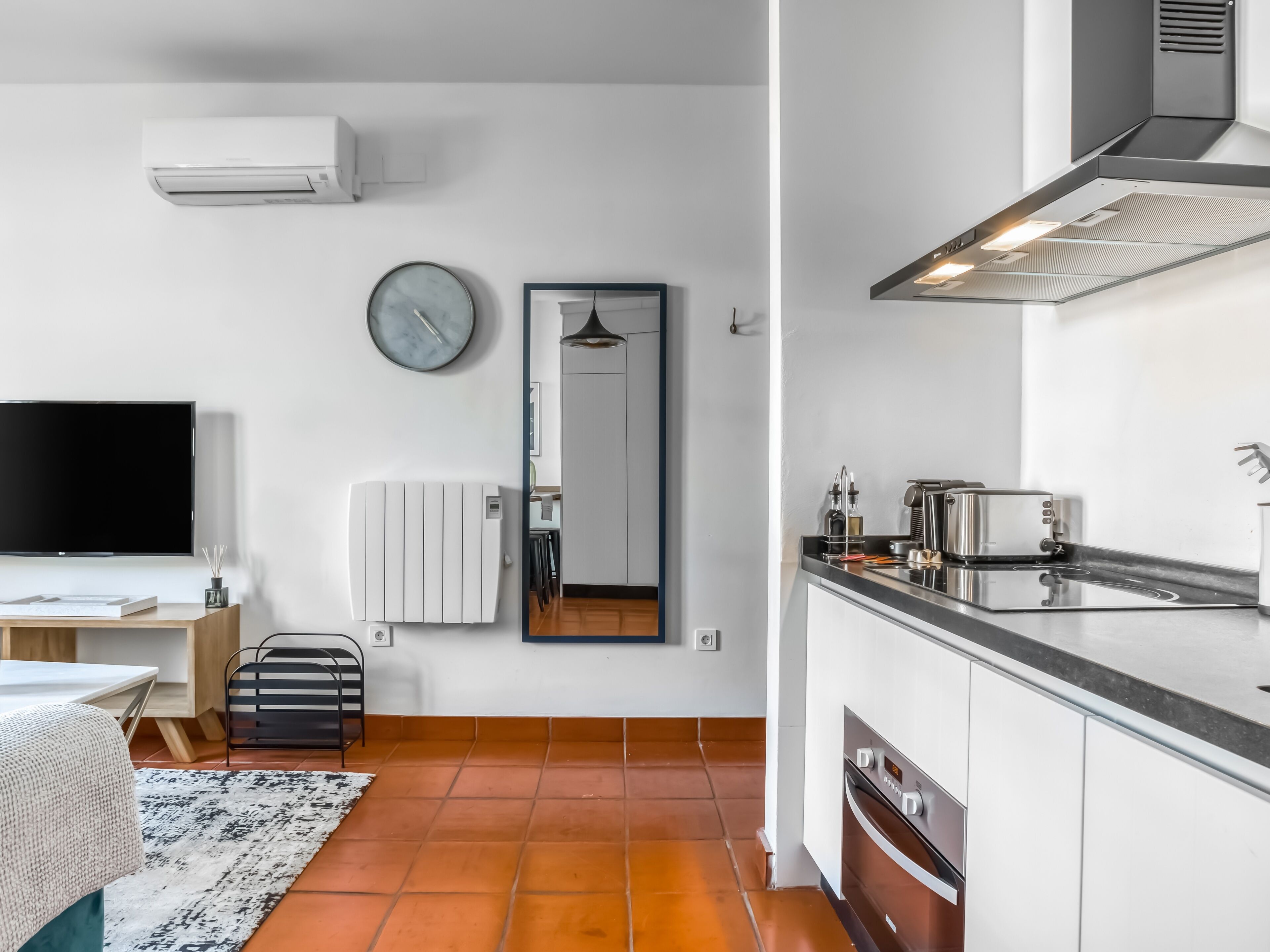 A modern kitchen with a stove, oven, and sink. There is a dining area with a table and chairs. A large flat-screen TV is mounted on the wall.