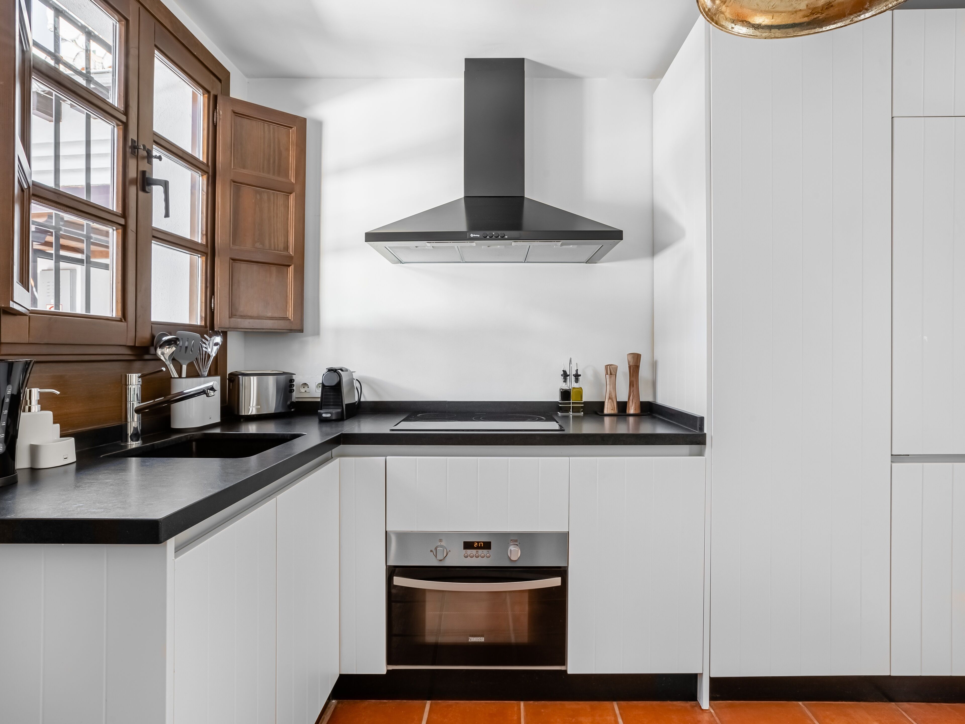 Eine moderne Küche mit weißen Schränken, einer schwarzen Arbeitsplatte, einem Edelstahlbackofen und Holzkorpussen.