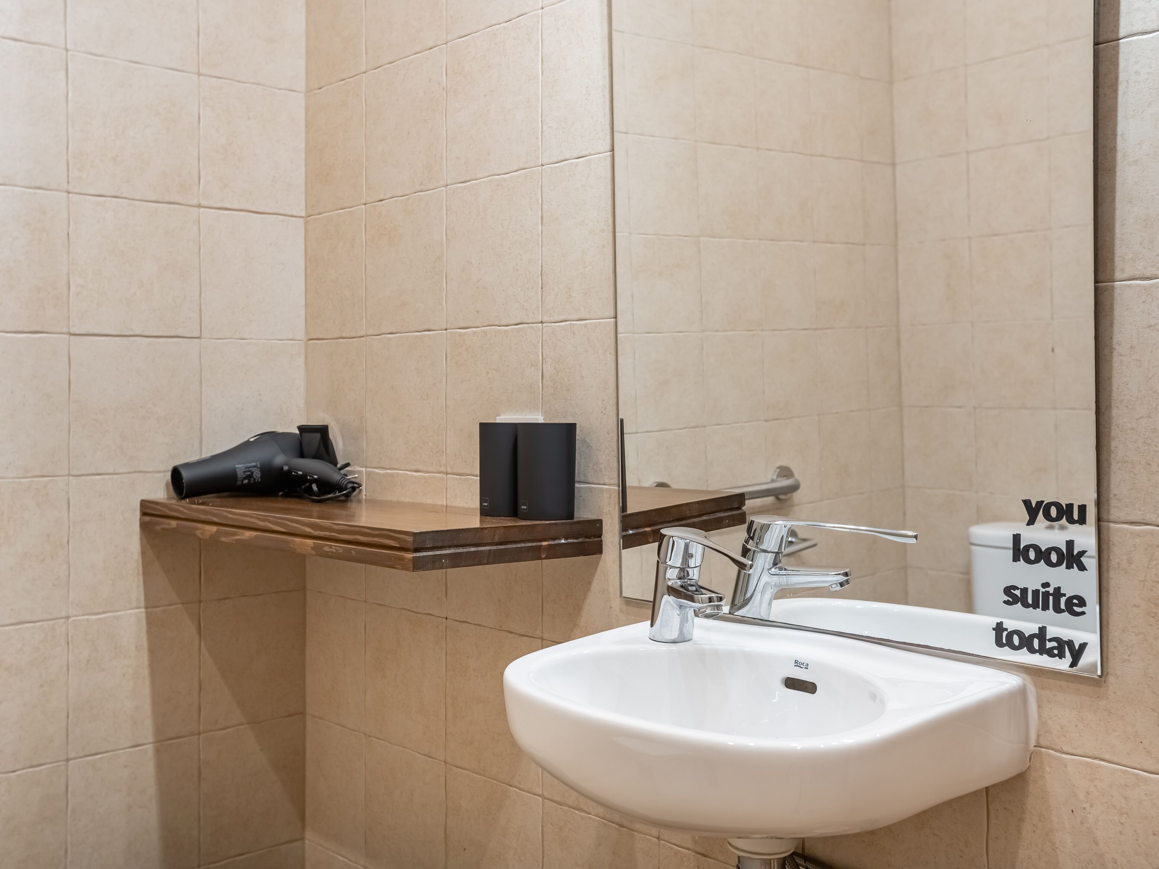 A bathroom with a white sink, a mirror, and a shelf with a hairdryer and a box.
