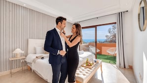 Une chambre moderne avec un grand lit, une vue sur la mer et un balcon avec un coin salon extérieur.