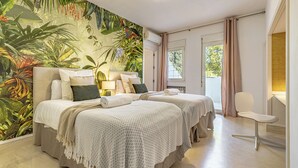 A hotel room with a large tropical mural, two beds with matching linens, a bedside table with a lamp, a chair, and a view of the outdoors through a window. - ELEGANT VILLA FOR GOLFERS: OUTDOOR BBQ, POOL AND SOLARIUM, PLUS HOME CINEMA ROOM (San Pedro de Alcántara)