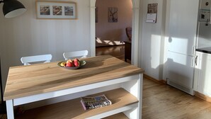 A dining area with a wooden table, two white chairs, and a bowl of fruit. There is a white refrigerator and a black lamp in the room. - Ferienhaus in Skruv am Bade- und Angelsee (Skruv)