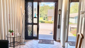 A room with a large glass door leading outside, a small round table with a plant, and a black chair. - Ferienhaus in Skruv am Bade- und Angelsee (Skruv)