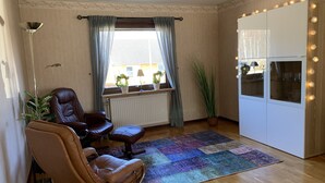 A cozy living room with a brown leather sofa, a small coffee table, a colorful rug, a potted plant, and a white cabinet with string lights. - Ferienhaus in Skruv am Bade- und Angelsee (Skruv)