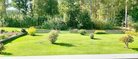 Un jardín bien cuidado con una terraza de madera, rodeado de árboles altos y diversos arbustos.