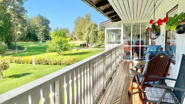 A wooden deck with a white railing, outdoor furniture, and a view of a green landscape. - Ferienhaus in Skruv am Bade- und Angelsee (Skruv)
