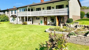 A two-story house with a balcony, a well-maintained lawn, and a stone retaining wall. - Ferienhaus in Skruv am Bade- und Angelsee (Skruv)