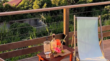 A wooden deck with a table set for two, overlooking a coastal area with a beach and a hill.