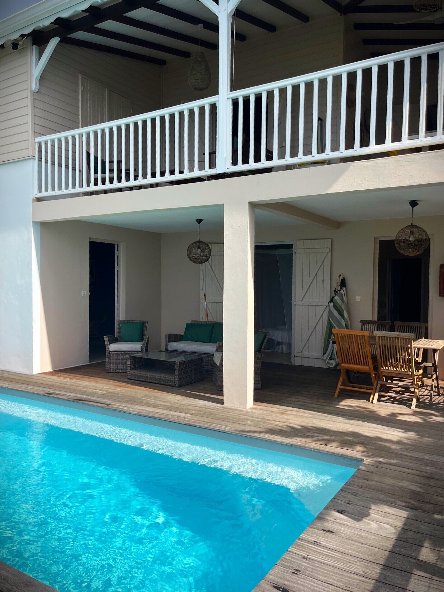 A two-story house with a wooden deck, a swimming pool, outdoor furniture, and a covered patio area.