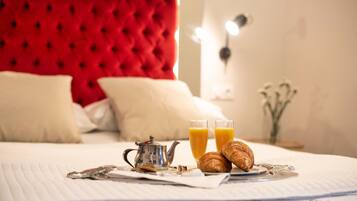 A neatly made bed with a red headboard, a teapot, two glasses of orange juice, and croissants on a white linen.