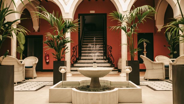 A courtyard with a central fountain, surrounded by potted plants and wicker furniture. - Palacio de San Fernando (Utrera)