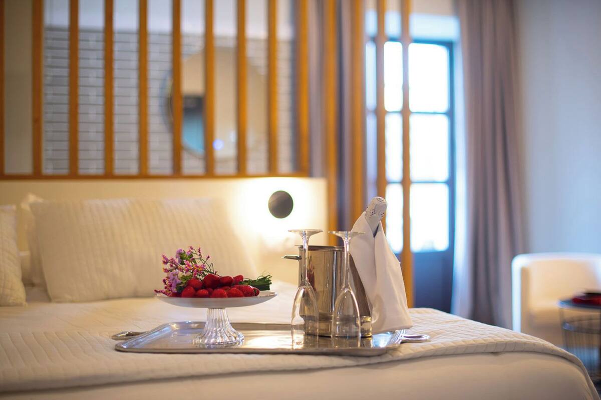A neatly made bed with a tray of strawberries and a pitcher of water, a glass, and a napkin on a hotel room.