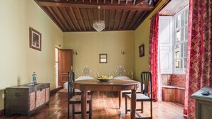Een eetruimte met een houten tafel, stoelen, een kroonluchter en een raam met gordijnen.