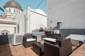 Une terrasse sur le toit, aménagée avec des meubles en osier, un climatiseur blanc et offrant une vue sur un bâtiment blanc doté d’un dôme et de fenêtres en arc de cercle.