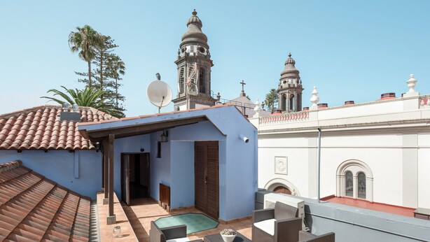 Een terras op het dak met rieten meubilair, een schotelantenne en uitzicht op een kerk met koepels.