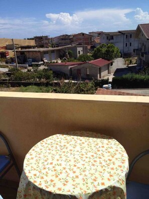 A balcony with a small round table covered in a floral tablecloth, overlooking a residential area with houses and a clear sky.
