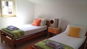 Two single beds with wooden frames, each with a pillow and a folded blanket. There is a small bedside table with a mirror and a lamp on one side. A red floral rug is on the floor between the beds. - Serenity Escape in Marina Di Caulonia (Caulonia)