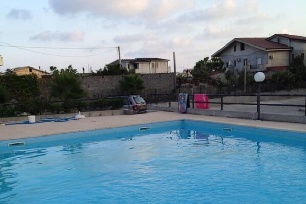 A swimming pool with a stone wall and a parked car nearby.