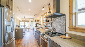 A modern kitchen with stainless steel appliances, a central island, and a stone backsplash. - Poolside Cabin #11 (3 bedroom cabin, Modern, Scenic Views, oversized deck.) (Kimberling City)