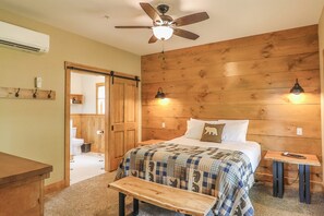 Ein Schlafzimmer mit hölzernem Kopfteil, einem Bett mit gemustertem Überwurf, einem Nachttisch, einer Bank, einem Deckenventilator und einer Wandleuchte.