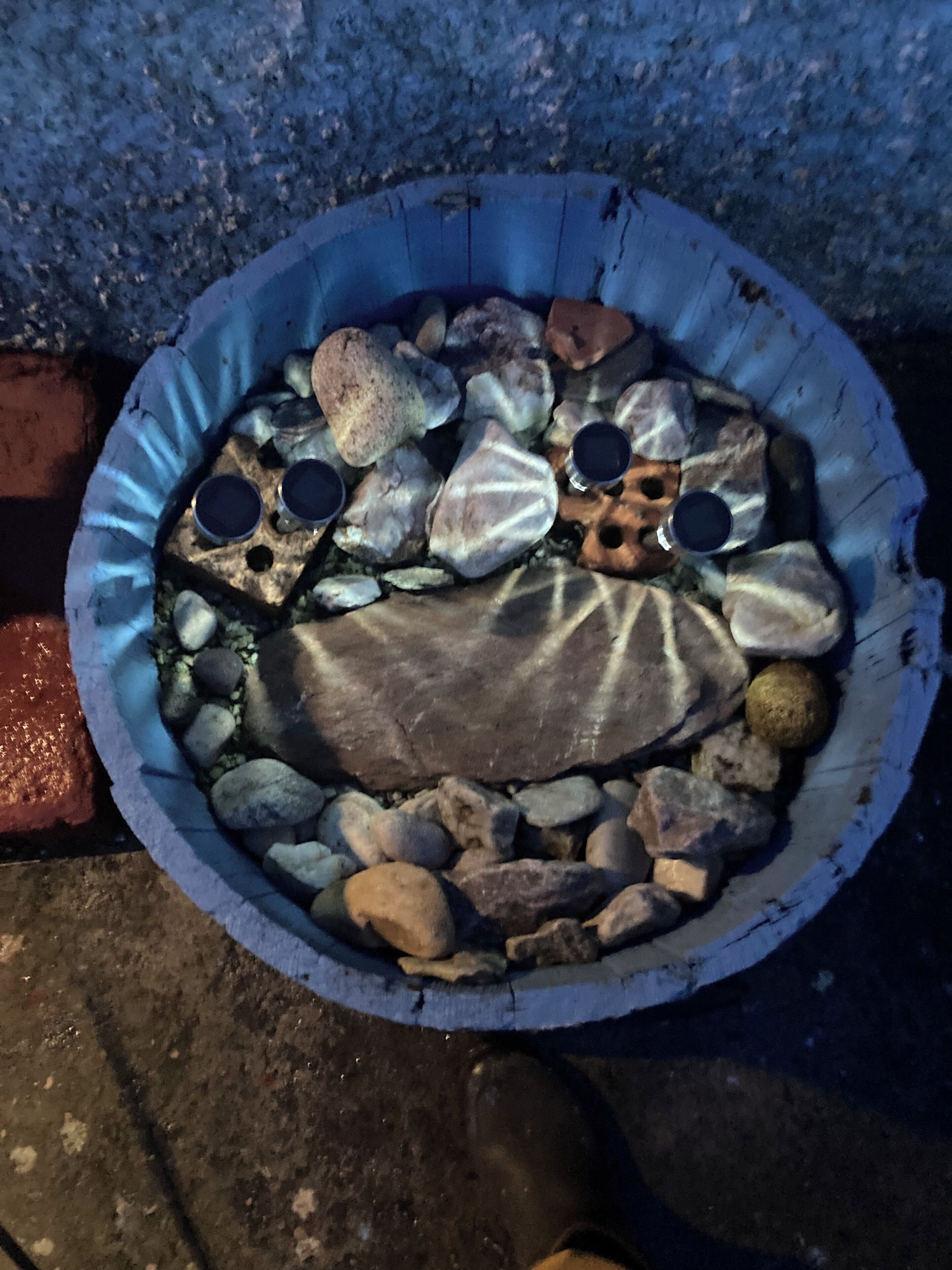 A round, shallow container filled with variously sized rocks and pebbles, some with holes.