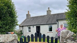 Une petite maison avec une porte en bois peinte en noir et une pancarte indiquant « Upper Imerval Cottage ».