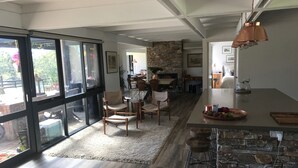 A modern kitchen with a stone backsplash, wooden chairs, and a large window overlooking a garden.