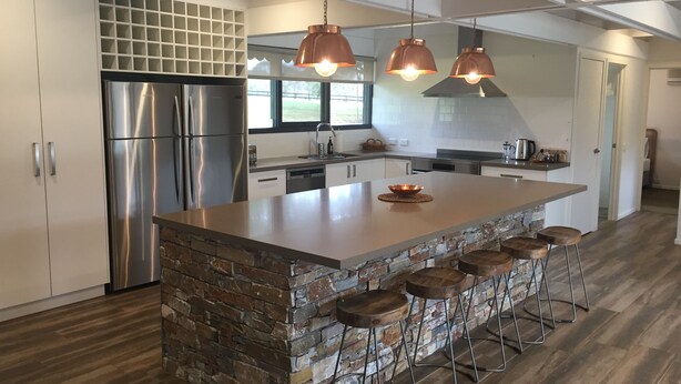 A modern kitchen with a central island, stainless steel appliances, and a stone accent wall.