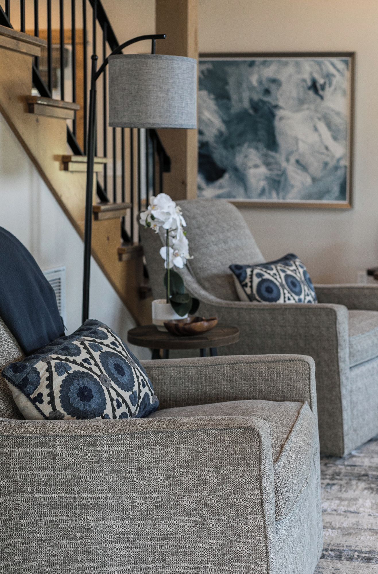 A living room with a staircase, a lamp, a painting, and patterned cushions.