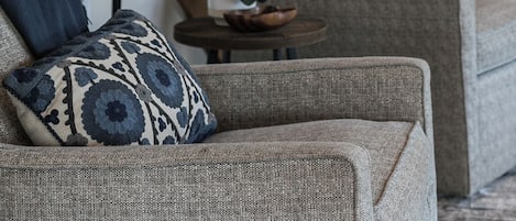 Una sala de estar con escalera, lámpara, un cuadro y cojines estampados.