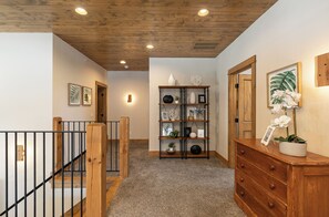 Un couloir avec un escalier en bois, une bibliothèque et une commode sur laquelle est posée une orchid ée en pot.