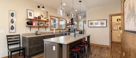 A modern kitchen with a central island, bar stools, pendant lighting, and wooden flooring.