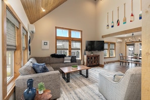 A spacious living room with a high ceiling, a television, and a dining area with a wooden table and chairs.