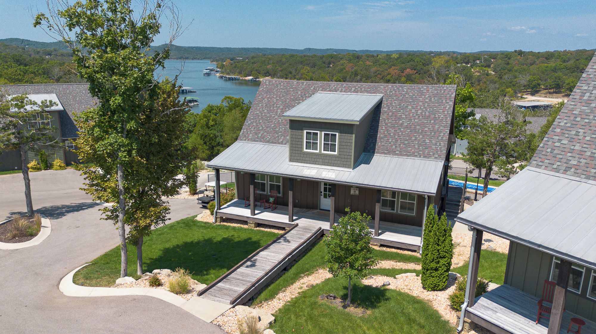 A two-story house with a covered porch, a small deck, and a view of a lake.